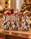 Three snow-dusted mini Christmas trees with curved tops, red baubles and bows, gold accents and rustic wooden bases; sold individually
