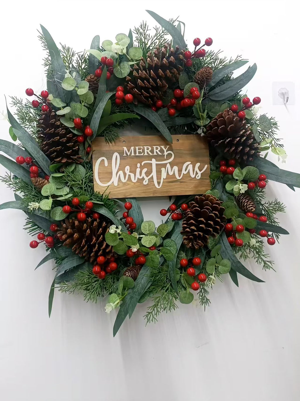 Green Christmas wreath with red berries, pine cones and a wooden-look Merry Christmas sign