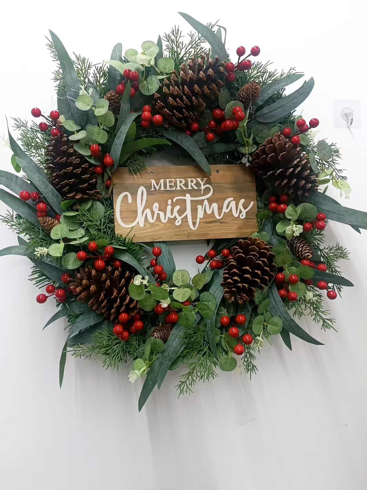 Green Christmas wreath with red berries, pine cones and a wooden-look Merry Christmas sign