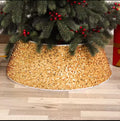Sparkling gold Christmas tree collar skirt covering the base of a tree with green branches and red berries