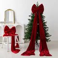 Oversized red bow with long draping ribbons styled on a Christmas tree beside a matching bow on a chair